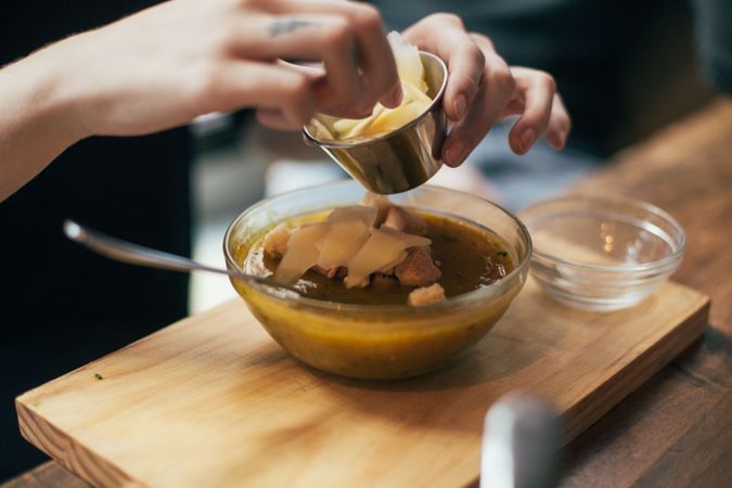 Person garnishing soup with cheese