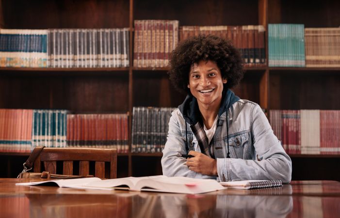 Happy biracial student studying in library and looking at camera