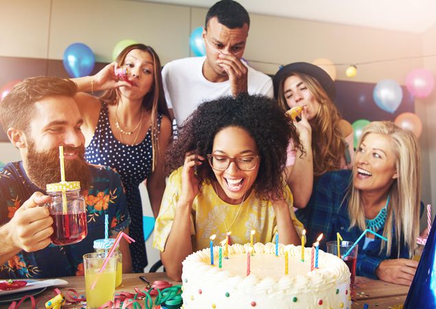 Happy group surrounding their friend as she blows out her birthday candles