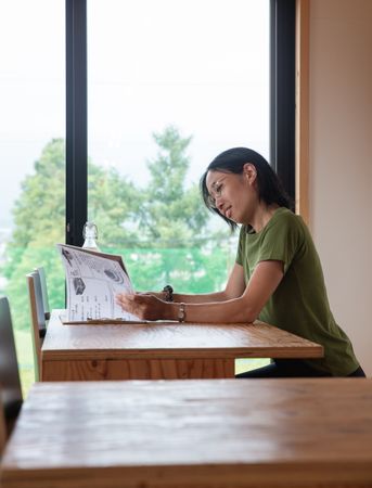 Woman in green shirt sitting at a table reading book