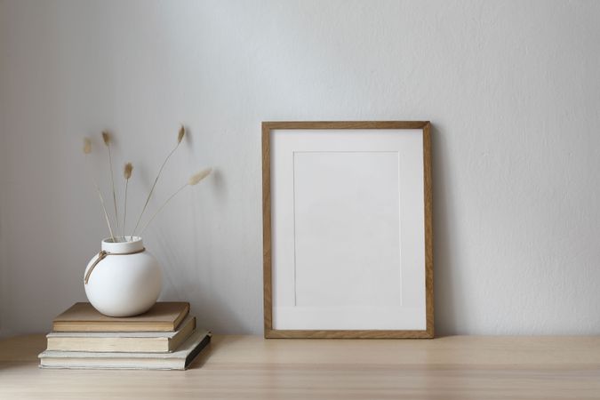 Vertical blank wooden picture frame mockup on table with modern round ceramic vase with dry bunny tails