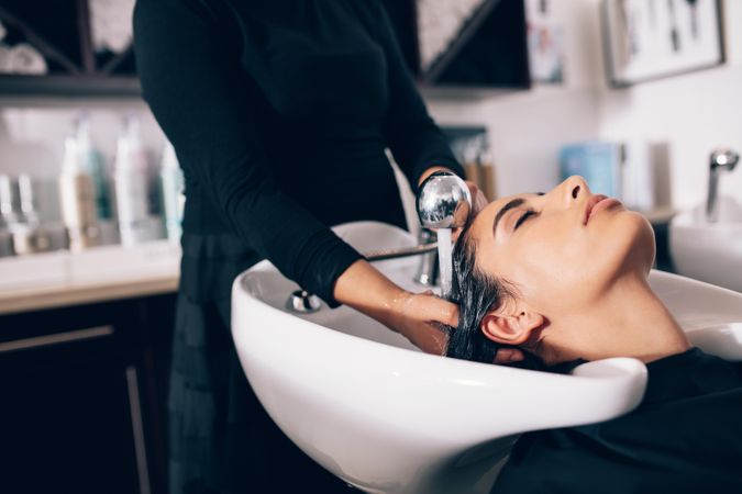 Close up of hairdresser washing customer’s hair in salon sink