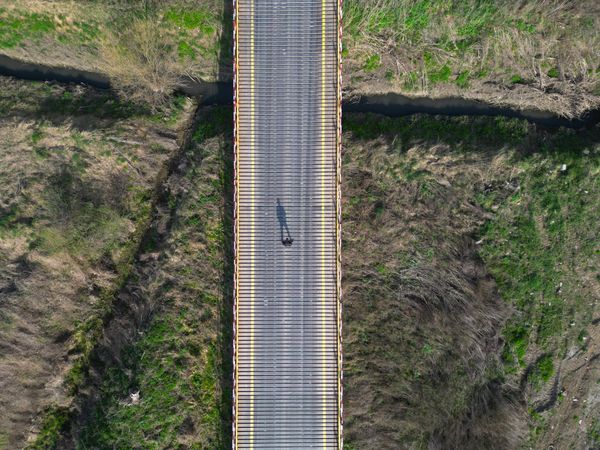 A single person is walking on the bridge, casting a long shadow due to the angle of sunlight