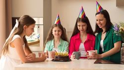 Family celebrating girl's birthday with cake and colorful party hats.