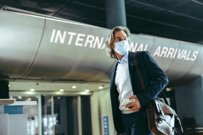 Businessman with face mask in front of international arrivals gate at airport