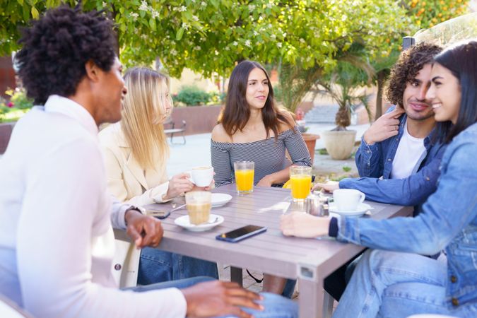 Male and female multi-ethnic friends smiling and talking outside with drinks