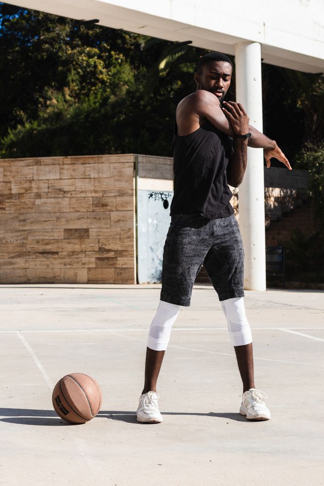 Black sportsman stretching on basketball court