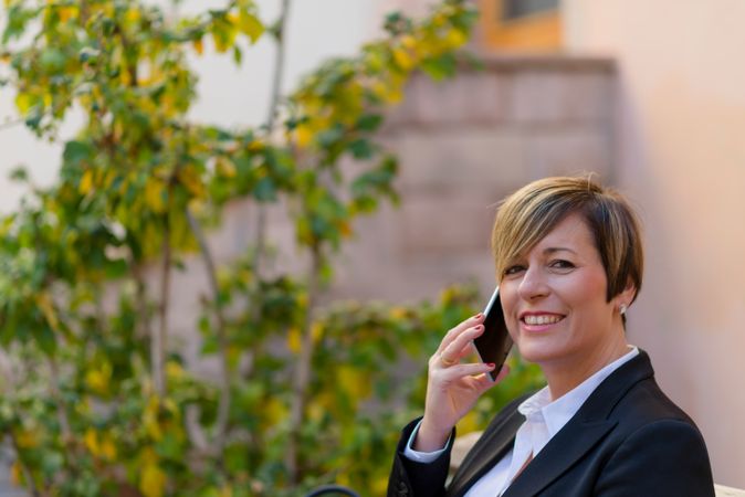 Portrait of woman in blazer speaking on phone with plant in background