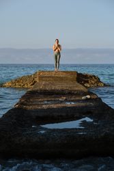 Slim woman standing on stone pier in sea