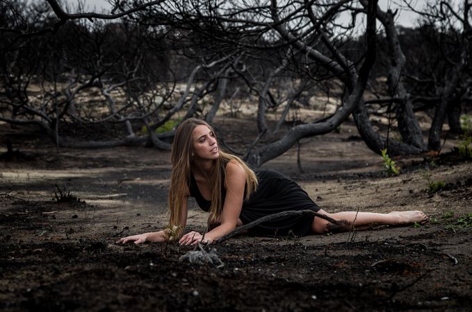 Woman posing on ground near dry trees