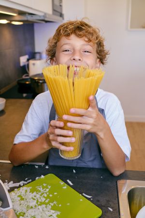 Smiling boy with raw spaghetti in house kitchen