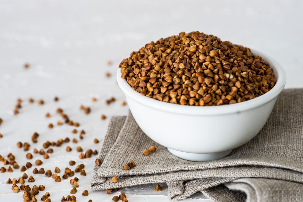 Organic raw buckwheat seeds in a bowl on wooden table with copy space