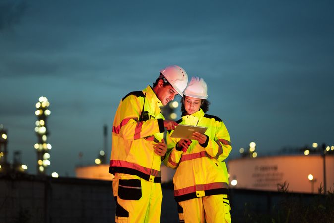 Team of two industrial workers reviewing a digital tablet at night