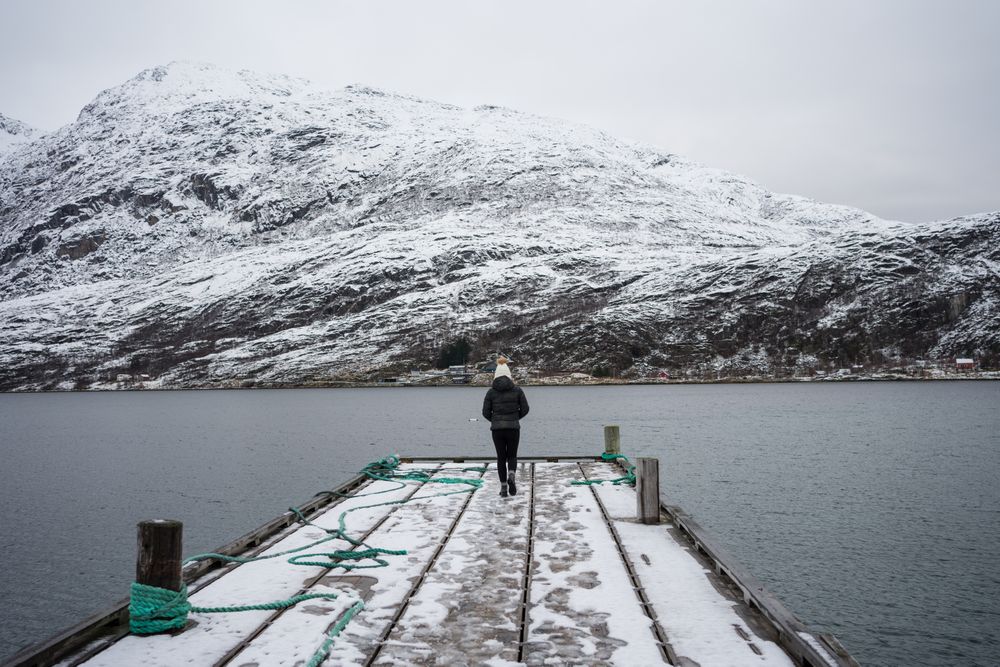 Woman on waterfront against small town at snowy foothill