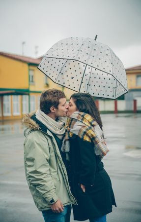 Man and woman kissing under dotted umbrella on rainy day