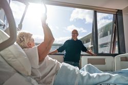 Aged man speaking with unhealthy wife lying on bed in clinic