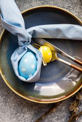 Easter holiday table setting with blue and yellow egg decorations in bowl with silverware