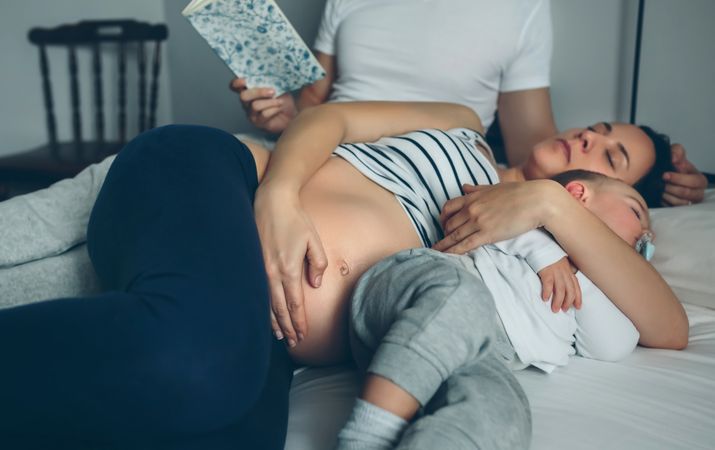 Man reading with pregnant wife and son sleeping