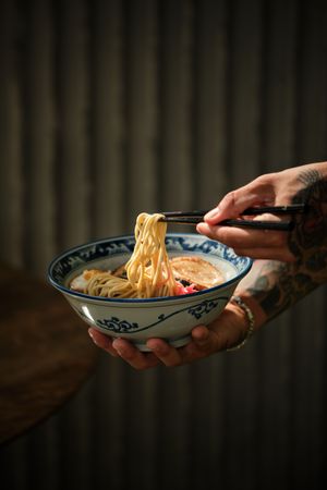 Crop person eating ramen noodles from bowl