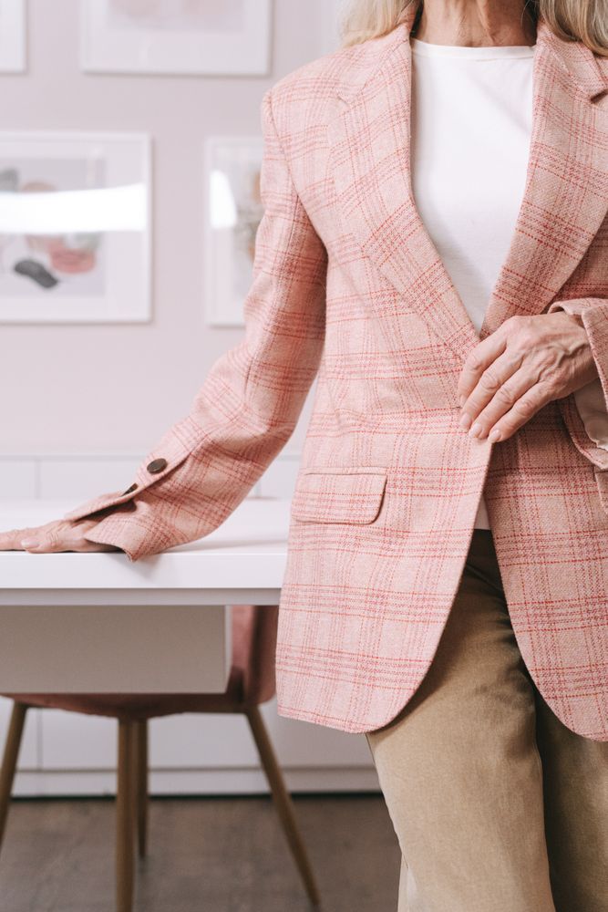 Woman in pink plaid blazer standing beside light desk indoor