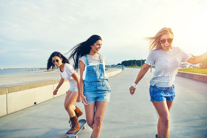 Happy female friends skateboarding on boardwalk near beach