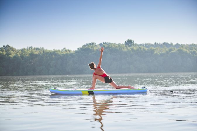 Woman stretching hips on paddleboard on lake in the morning