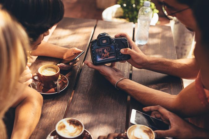 Man showing a picture on his dslr camera to friends sitting at cafe table