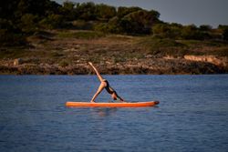 Sportswoman taking Downward Facing Dog pose on paddleboard in se