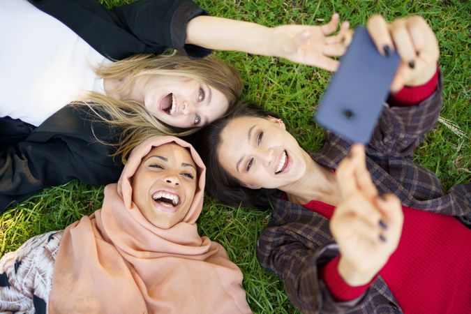 Looking down at three women lying back on grass with phone