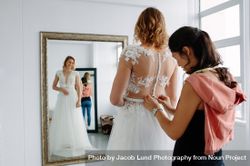 Woman assistant helping female in trying wedding dress in a shop bEePGb