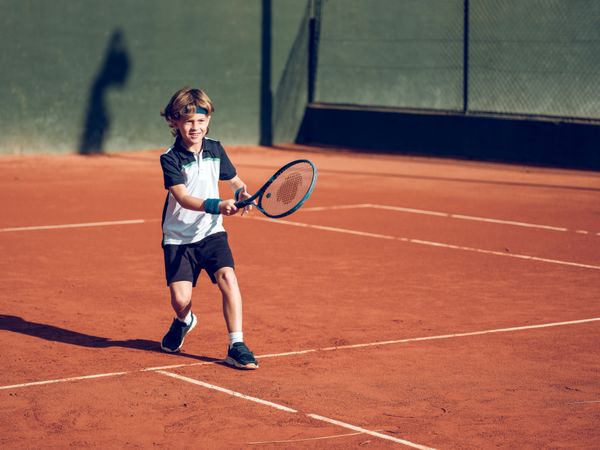 Adorable little boy running to hit ball while playing tennis