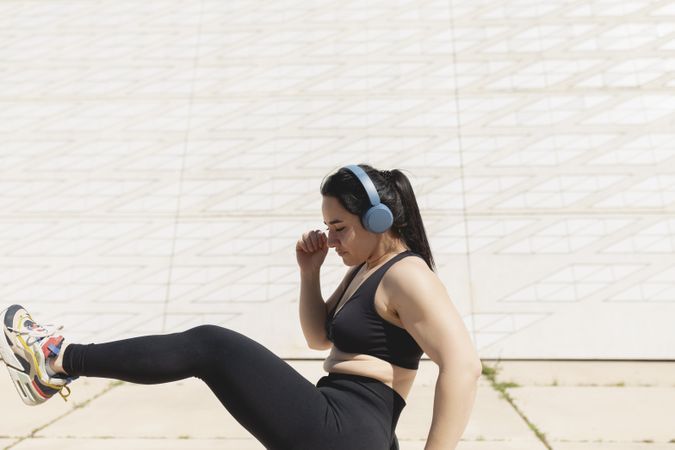 A woman kicks her leg in the air while listens to music in the sun after exercising