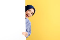 Happy Smiling Young Asian Muslim Woman with Hijab Peeking Out Behind a Wall