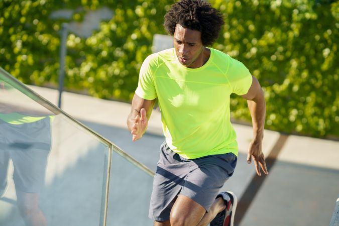 Healthy man with afro hair in neon T-shirt jogging up stairs
