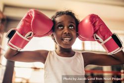 Girl wearing boxing gloves standing in a boxing ring touching her head with gloves and looking up. 5687jb