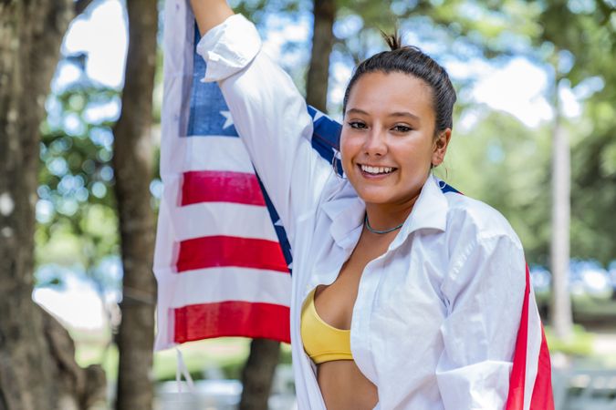 Content woman smiling wrapped in American flag walking along park