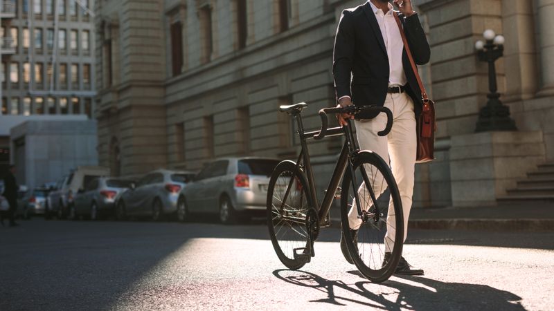 Cropped image of businessman walking on city street with a bicycle and talking on mobile phone