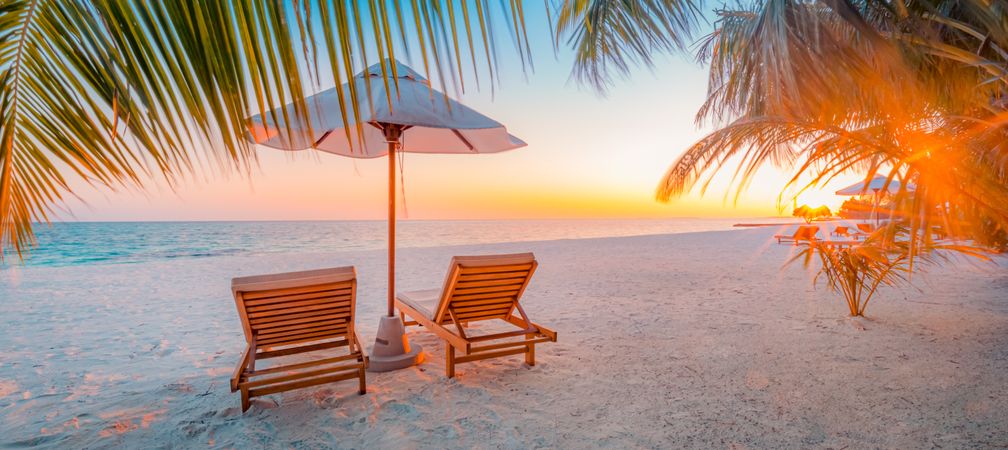 Wide shot of beach at sunset with sun flare and two beach chairs