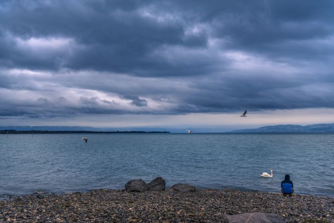 Man on a lake shore under stormy sky