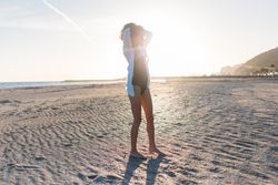 Woman with her arms up on beach at sunset in oversized shirt