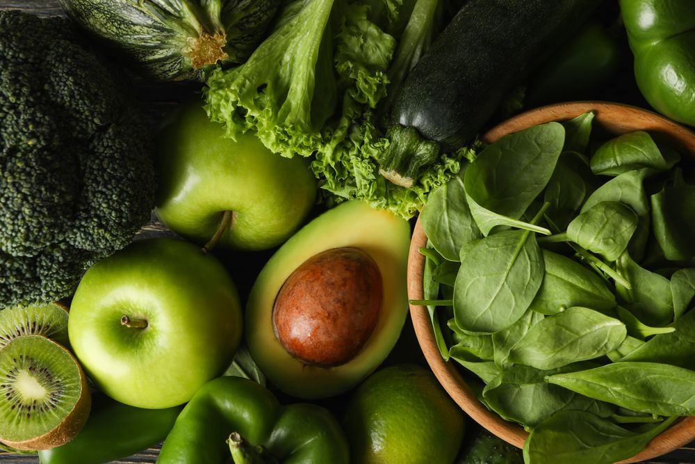 Green vegetables and fruits on wooden background, top view