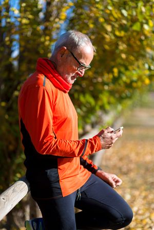 Male checking phone while leaning on wooden fence in park