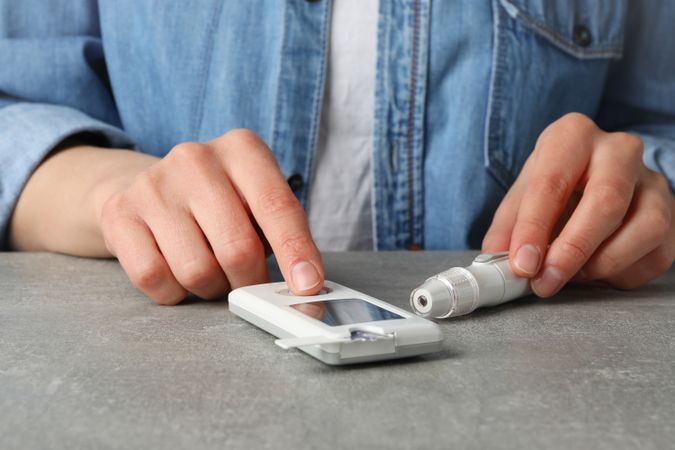 Woman uses blood sugar level test on gray table