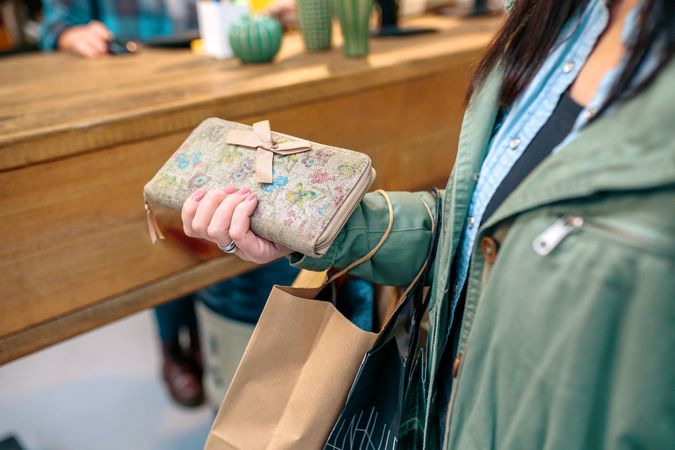 Unrecognizable woman client holding wallet with bow and ecological shopping paper bags on store