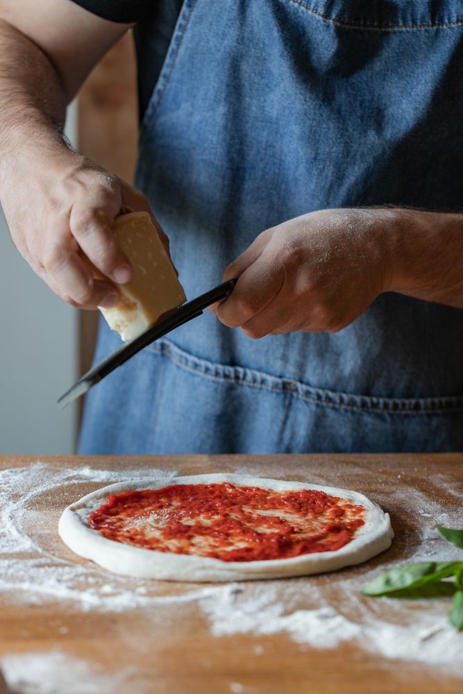 Crop cook grinding cheese on pizza