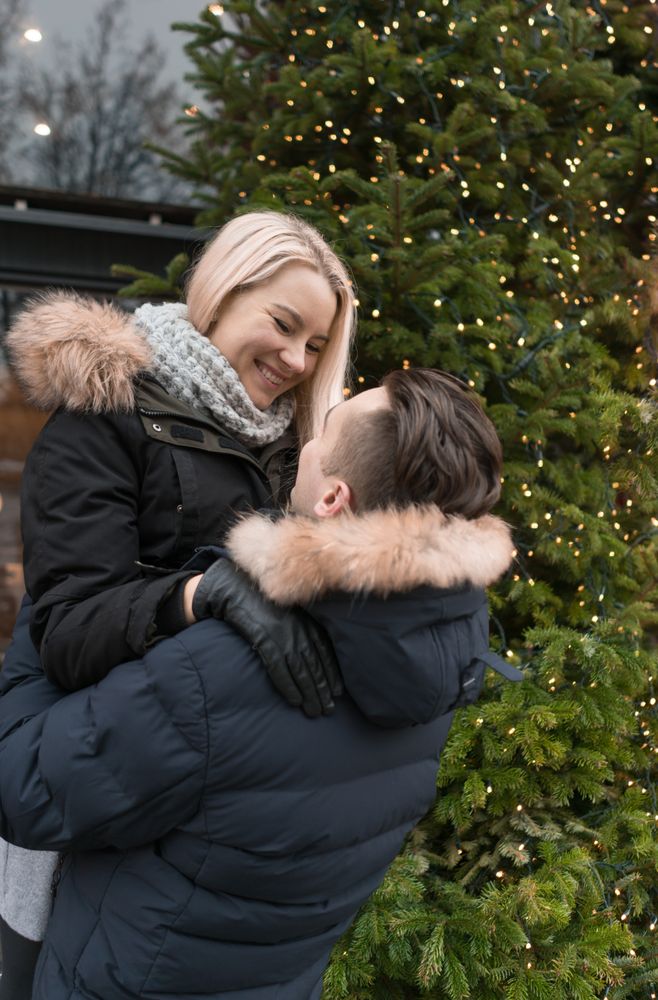 Smiling couple having fun on street near fir tree with fairy lights