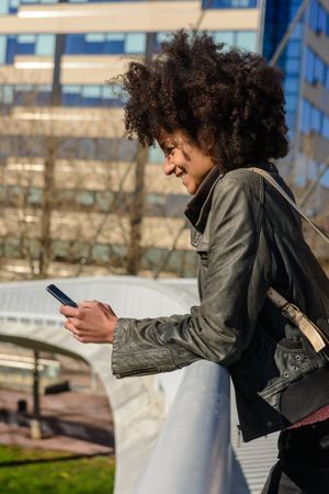 Woman with afro hair looking at her phone while walking.