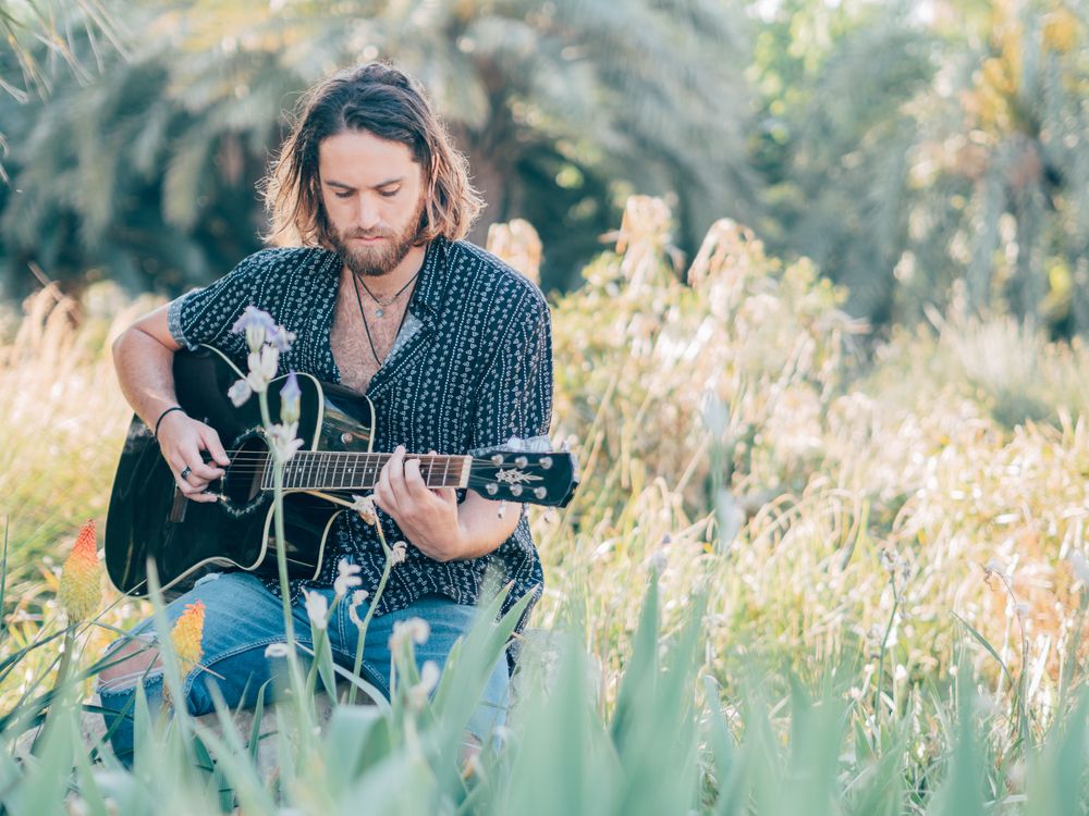 Hipster man in meadow with guitar