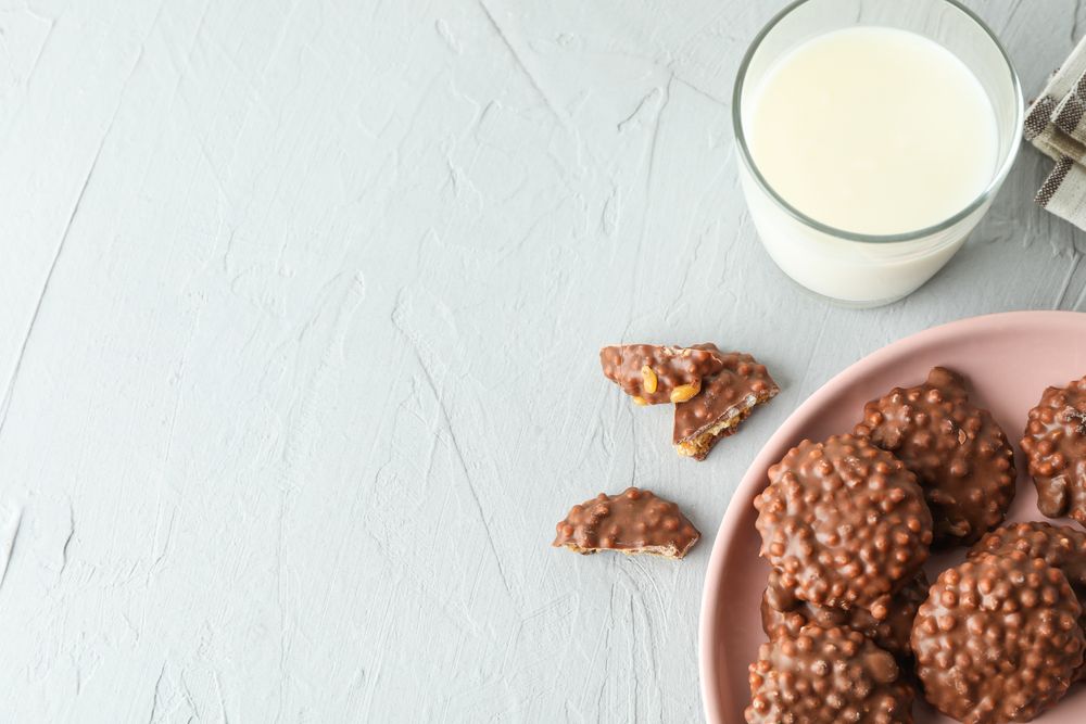 Plate with chocolate cookies and glass of milk on grey table, space for text