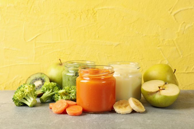 Composition with baby food on gray table against yellow background